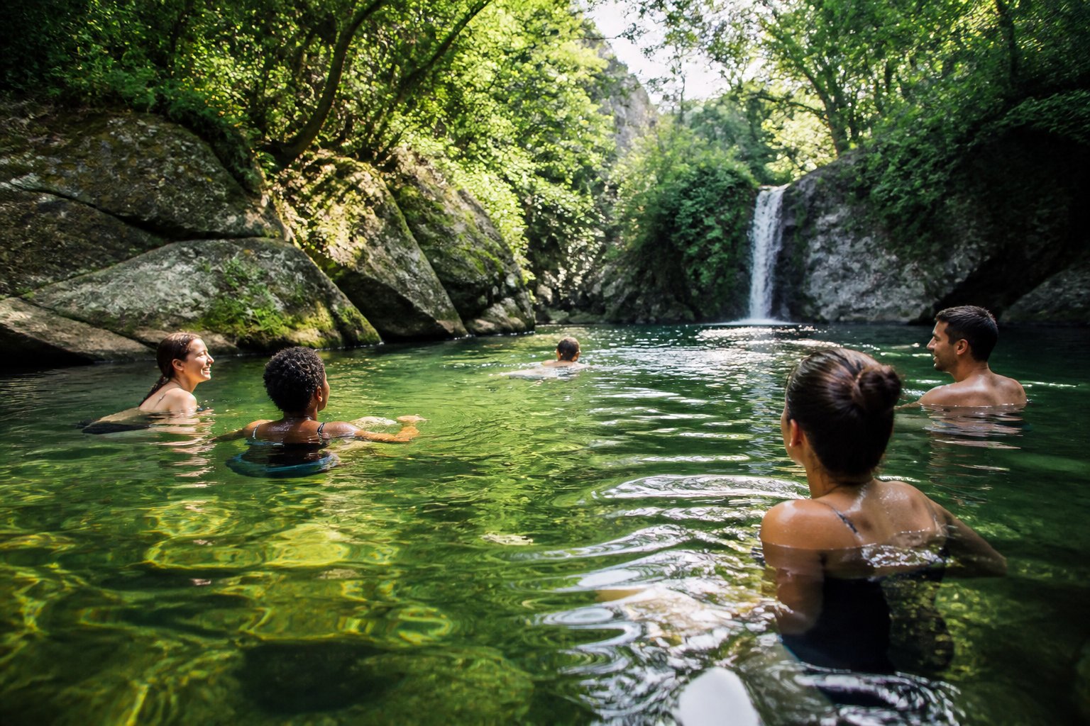 People swimming and enjoying a natural freshwater lake surrounded by trees and greenery on a sunny day.