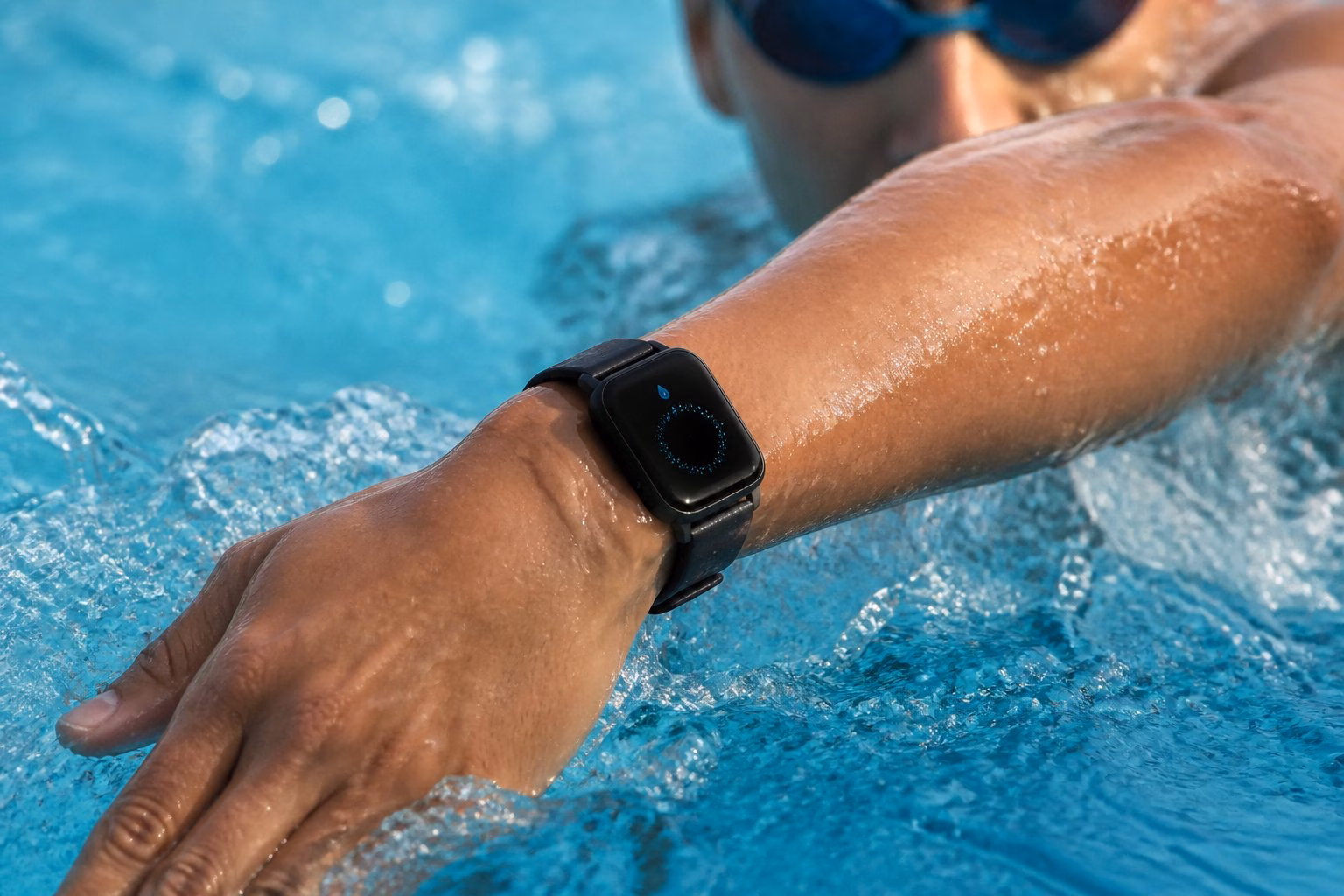 A person swimming in a pool wearing an Apple Watch on their wrist with water splashing around.