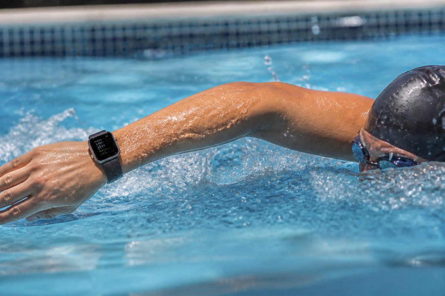 A person swimming in a pool wearing an Apple Watch on their wrist, with water droplets around their arm.
