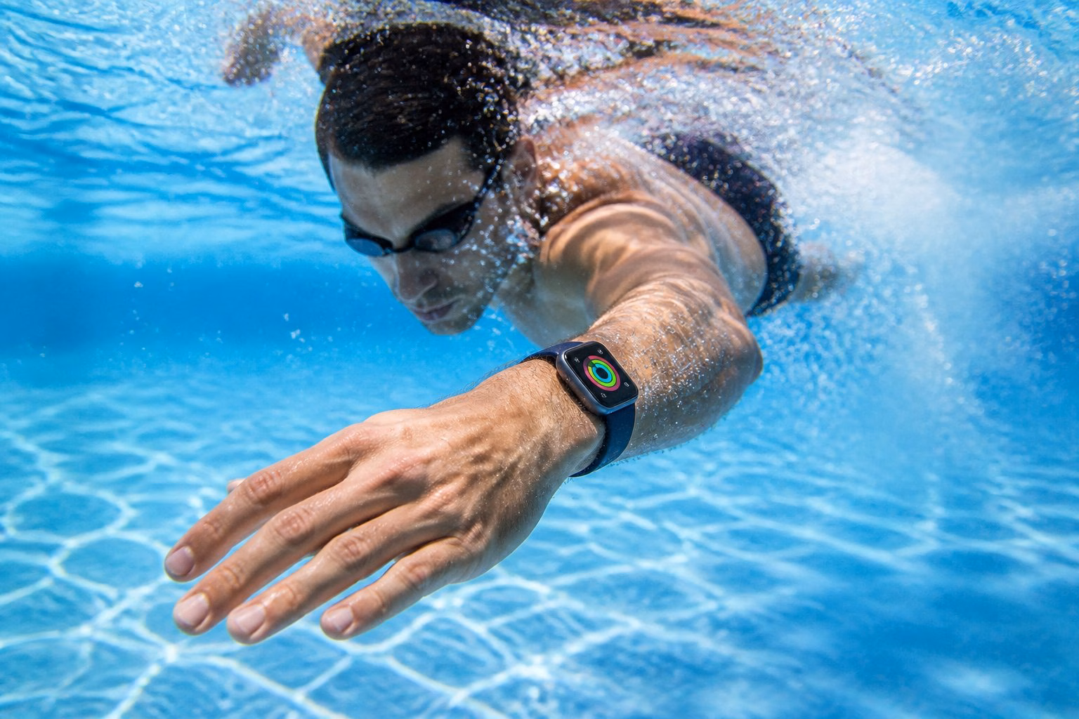 A person swimming underwater in a pool wearing an Apple Watch on their wrist.