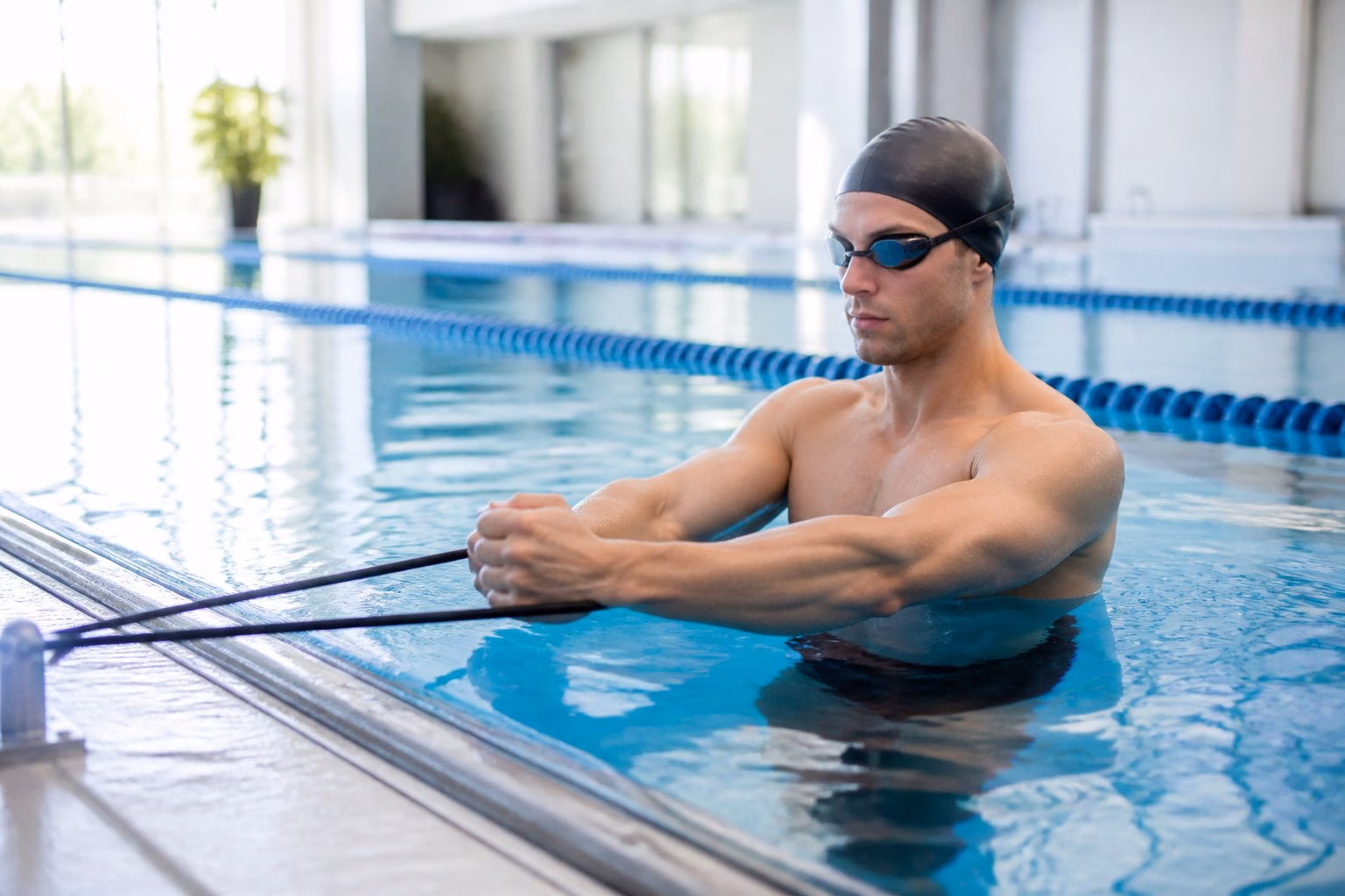 A swimmer in a swimming pool using resistance bands for strength training exercises.