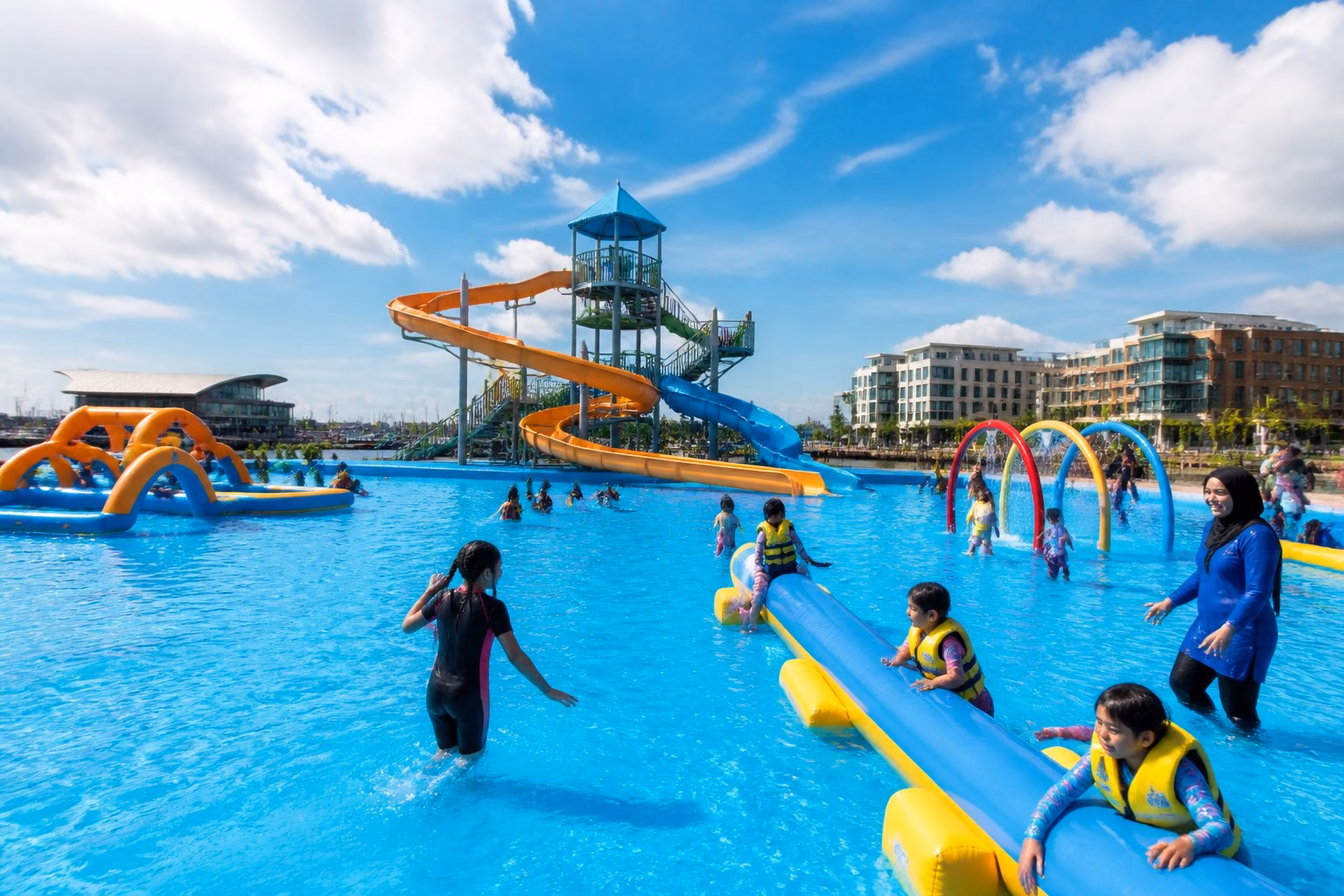 Families and children enjoying colourful water slides and inflatable obstacles at an aqua park beside Cardiff Bay.