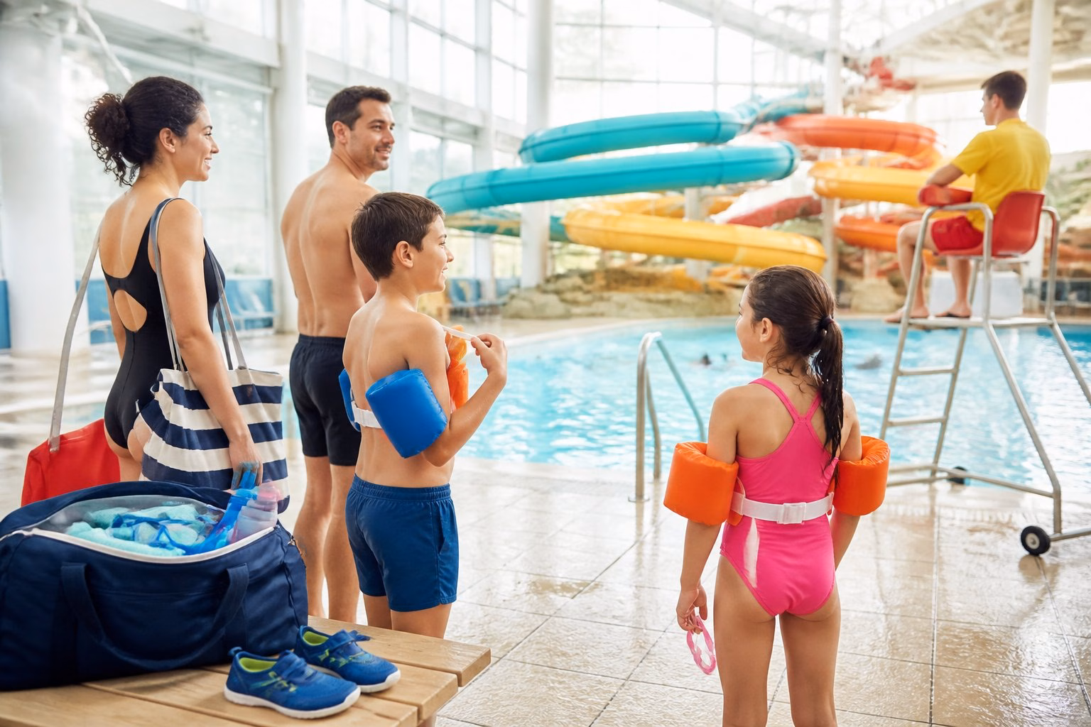 A family prepares for a day at an indoor aqua park while a lifeguard watches nearby.
