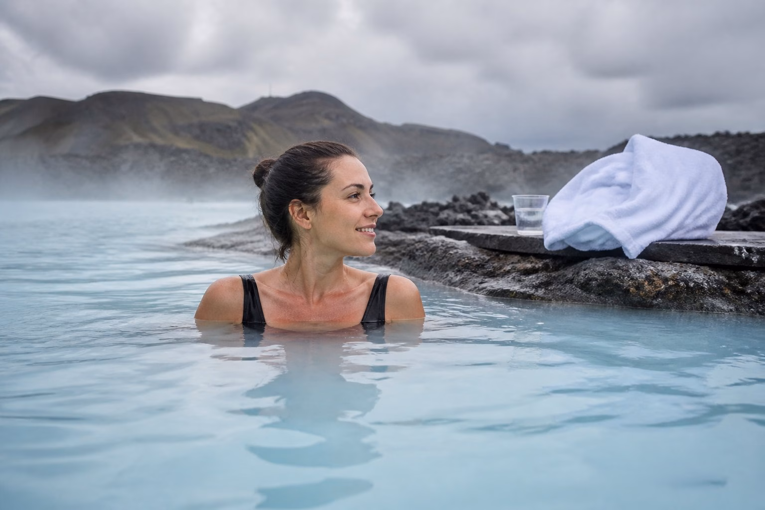 A swimmer relaxes in the warm turquoise waters of Iceland's Blue Lagoon, surrounded by dark volcanic rocks and gentle steam.