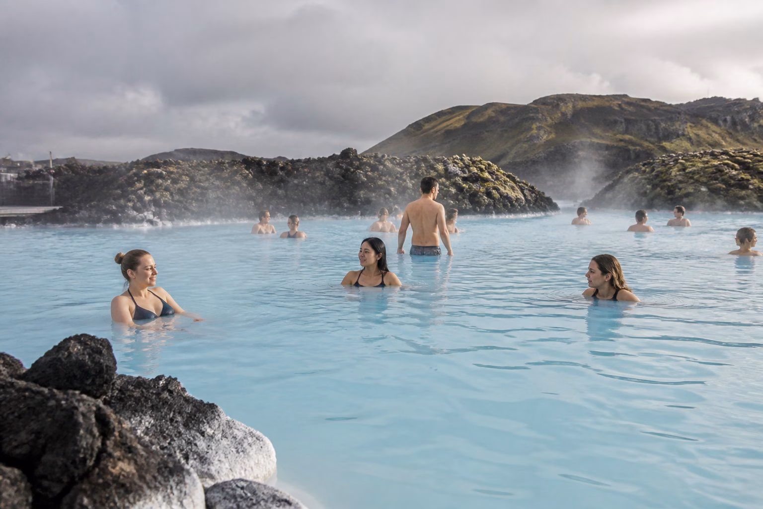 People relaxing in the blue geothermal waters of Iceland’s Blue Lagoon among volcanic rocks and steam.