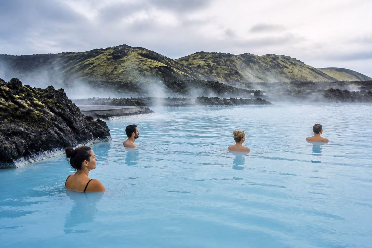 People calmly soaking in the milky blue waters of Iceland’s Blue Lagoon, surrounded by volcanic rocks and rising steam.