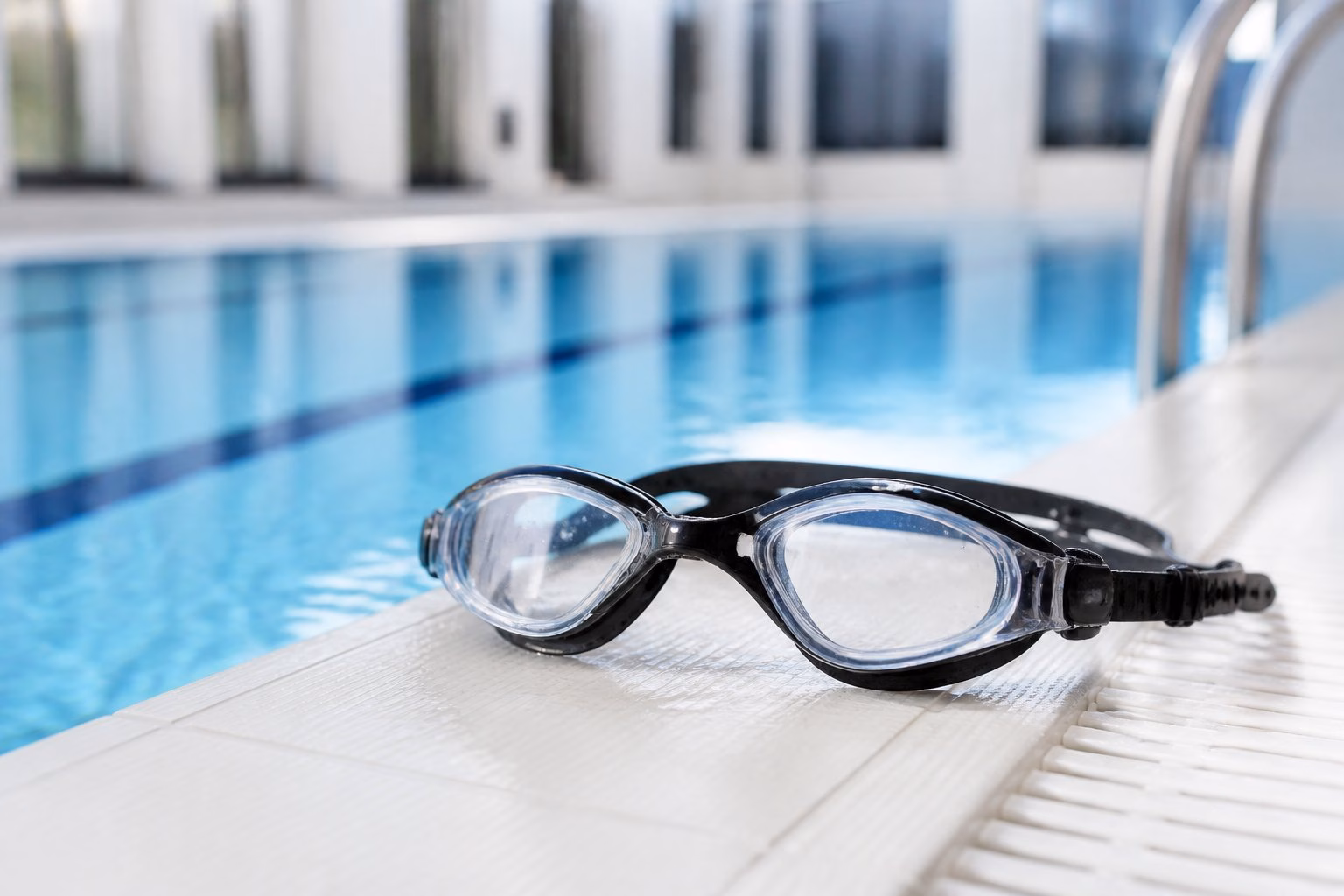 Prescription swimming goggles resting beside the edge of a blue indoor swimming pool.