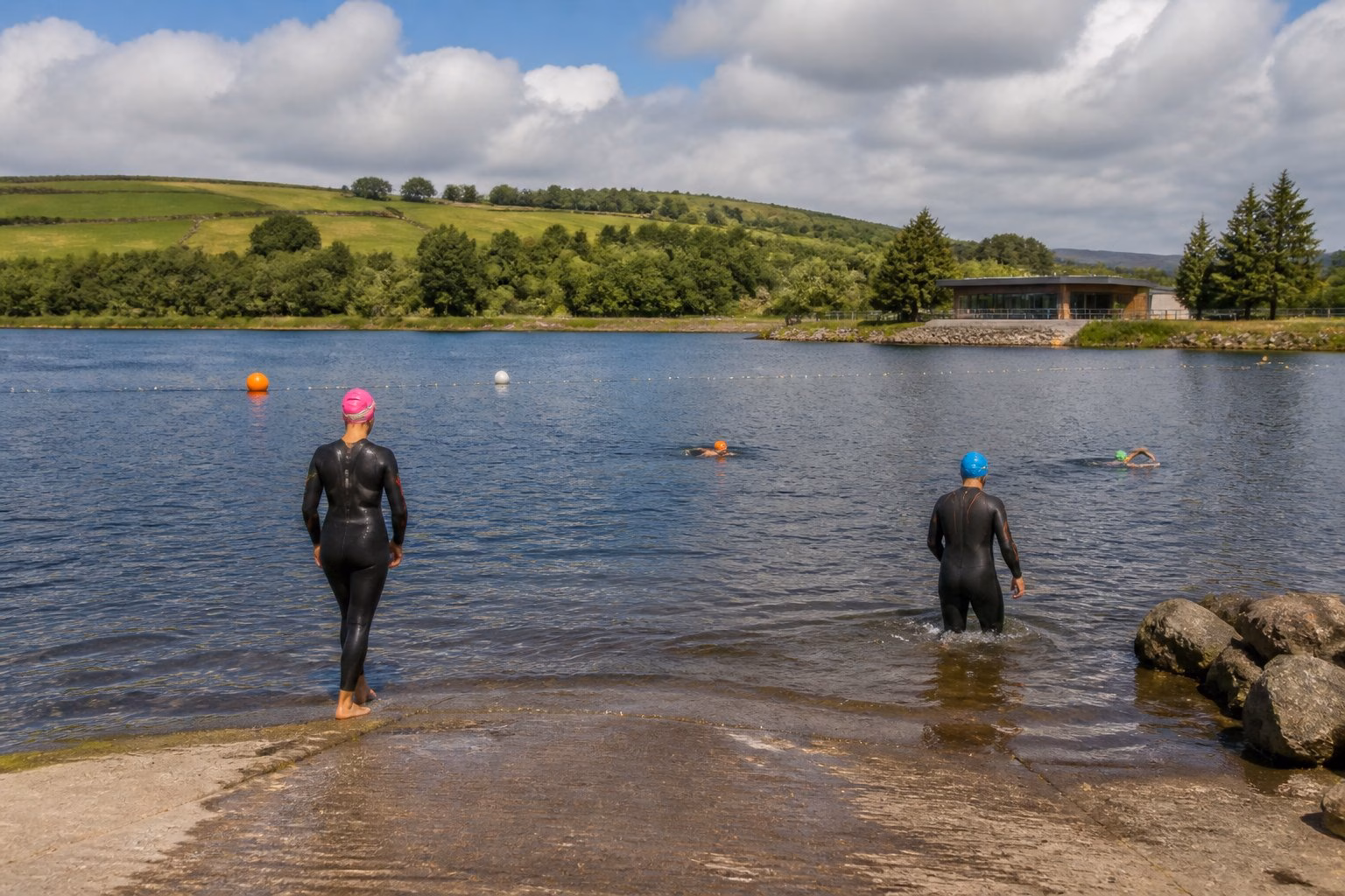 Swimmers using a calm, buoy-marked lake surrounded by green Yorkshire countryside.