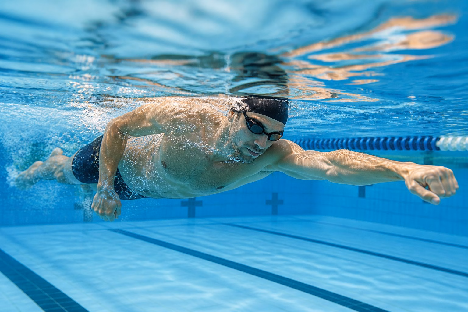 Swimmer practising a closed-fist freestyle drill underwater in a swimming pool.