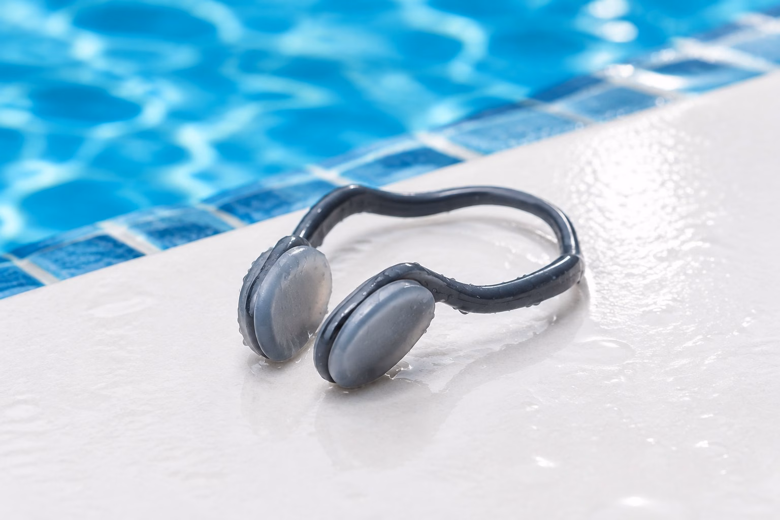 A swimming nose clip resting beside the edge of a blue swimming pool.
