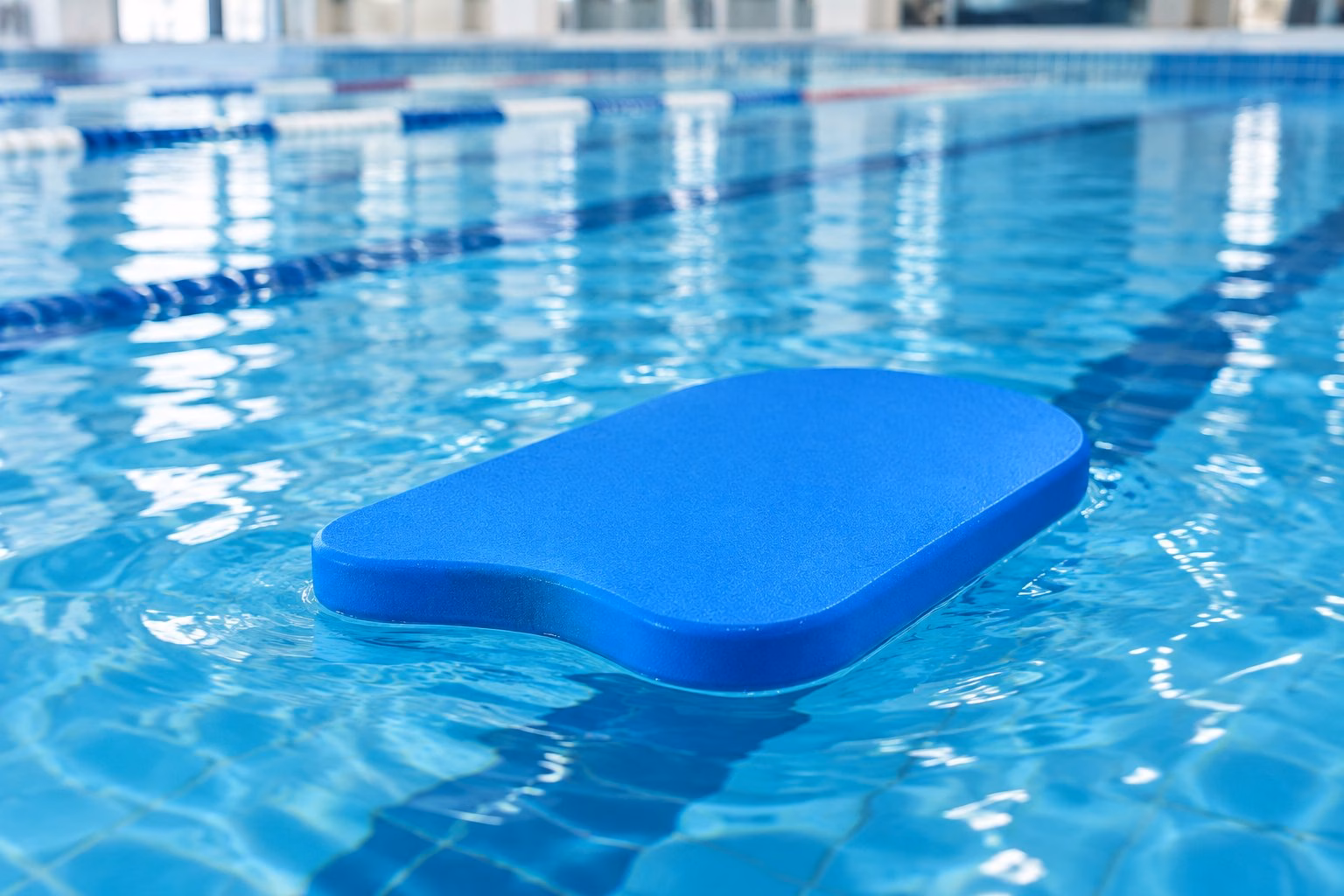 A foam swimming kickboard floating on the water in an indoor pool.