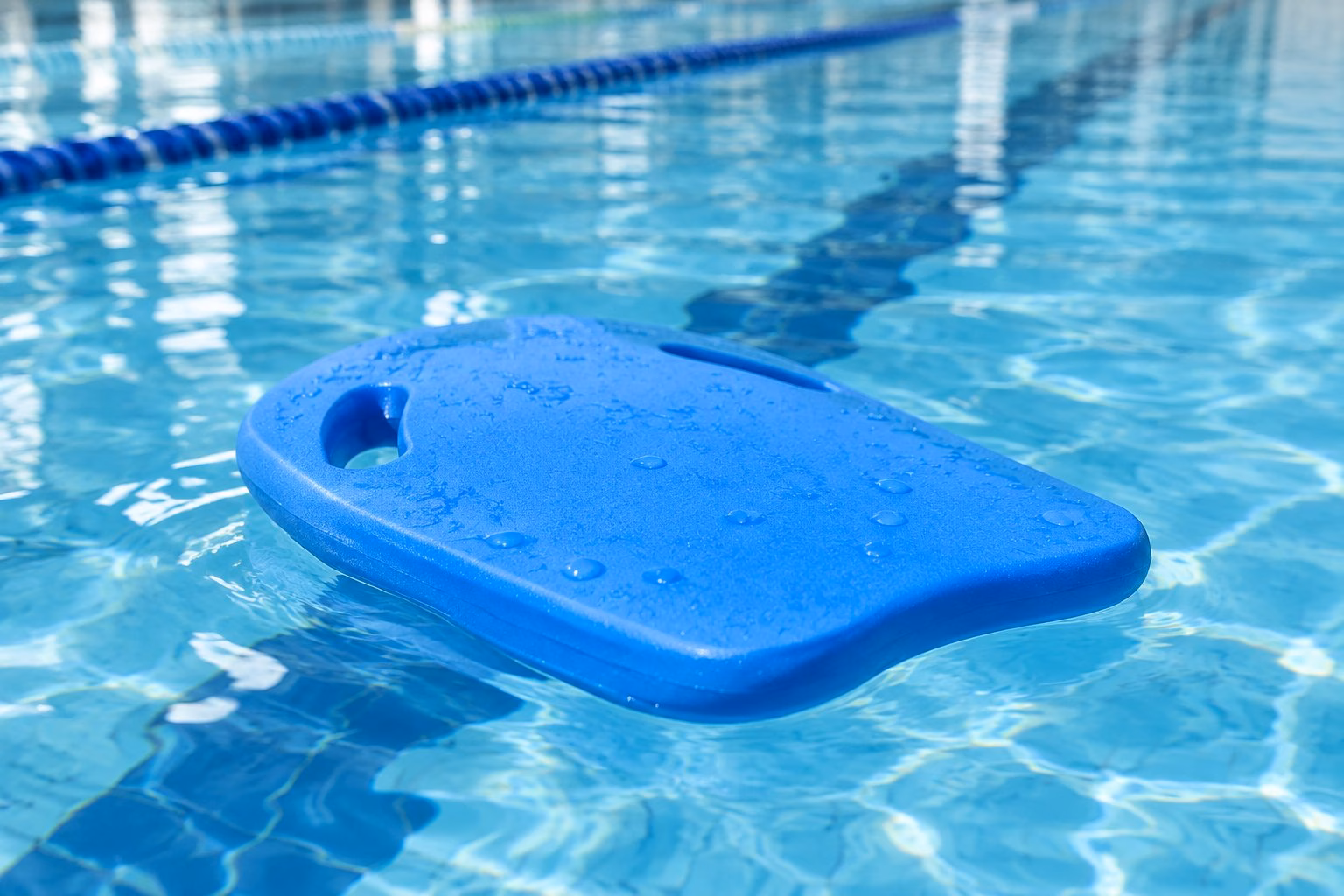 A blue swimming kickboard floating on the water in a pool.