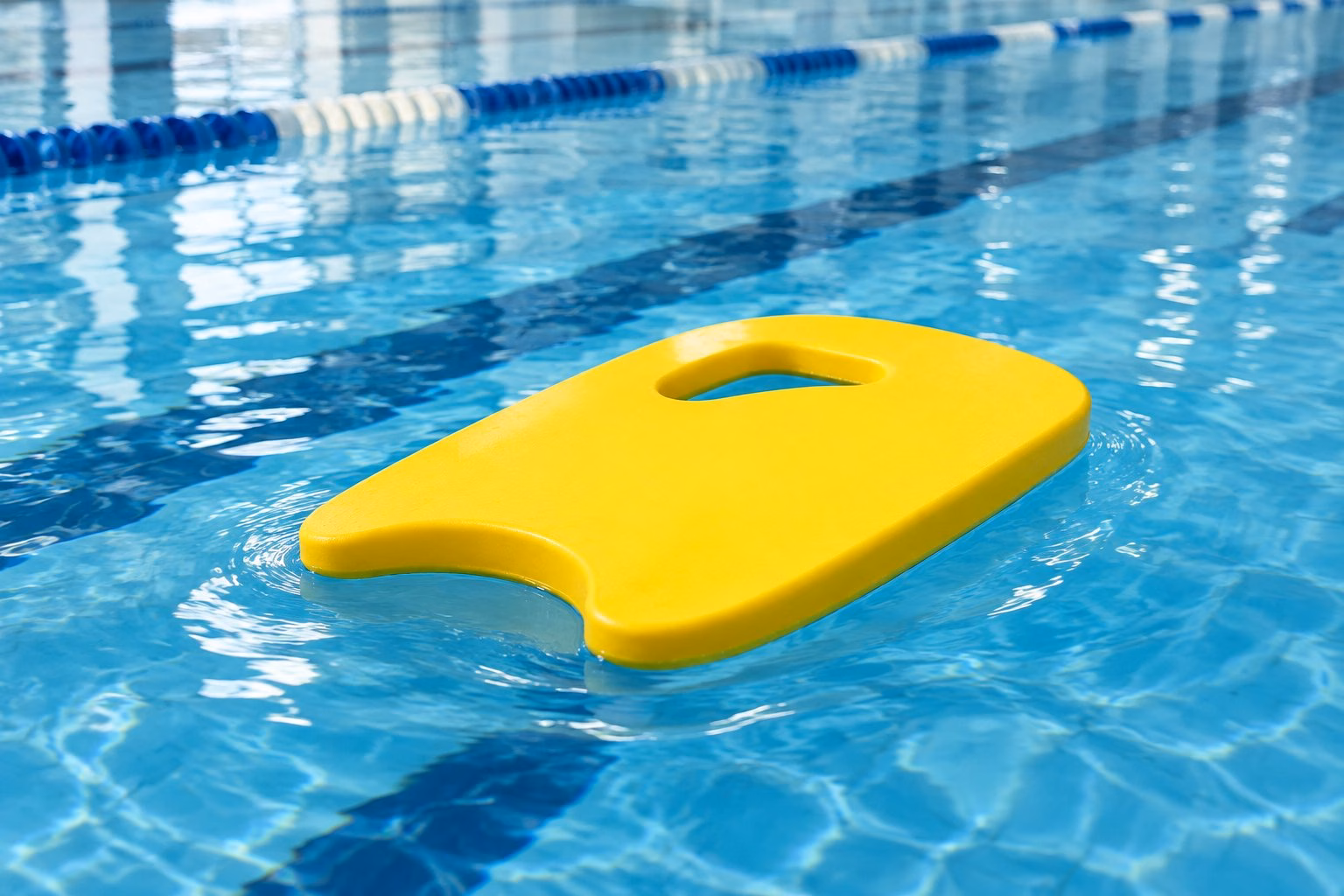 A bright yellow swimming kickboard floating on blue pool water.
