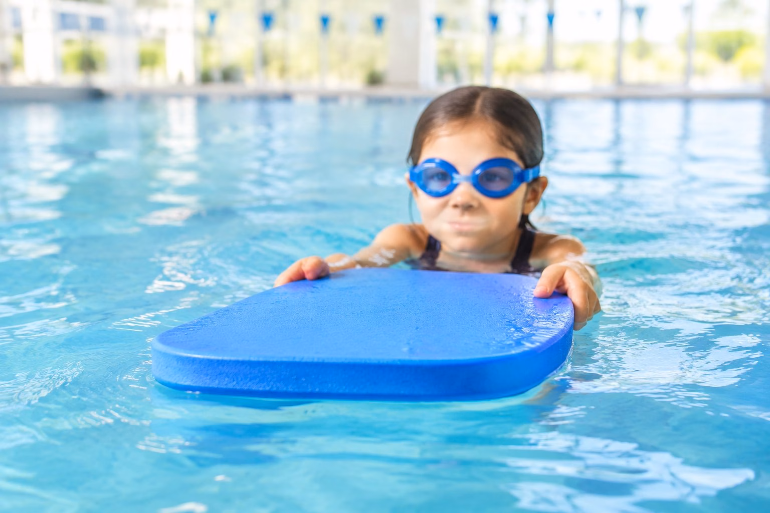 A young swimmer holds a colourful kickboard in a swimming pool.