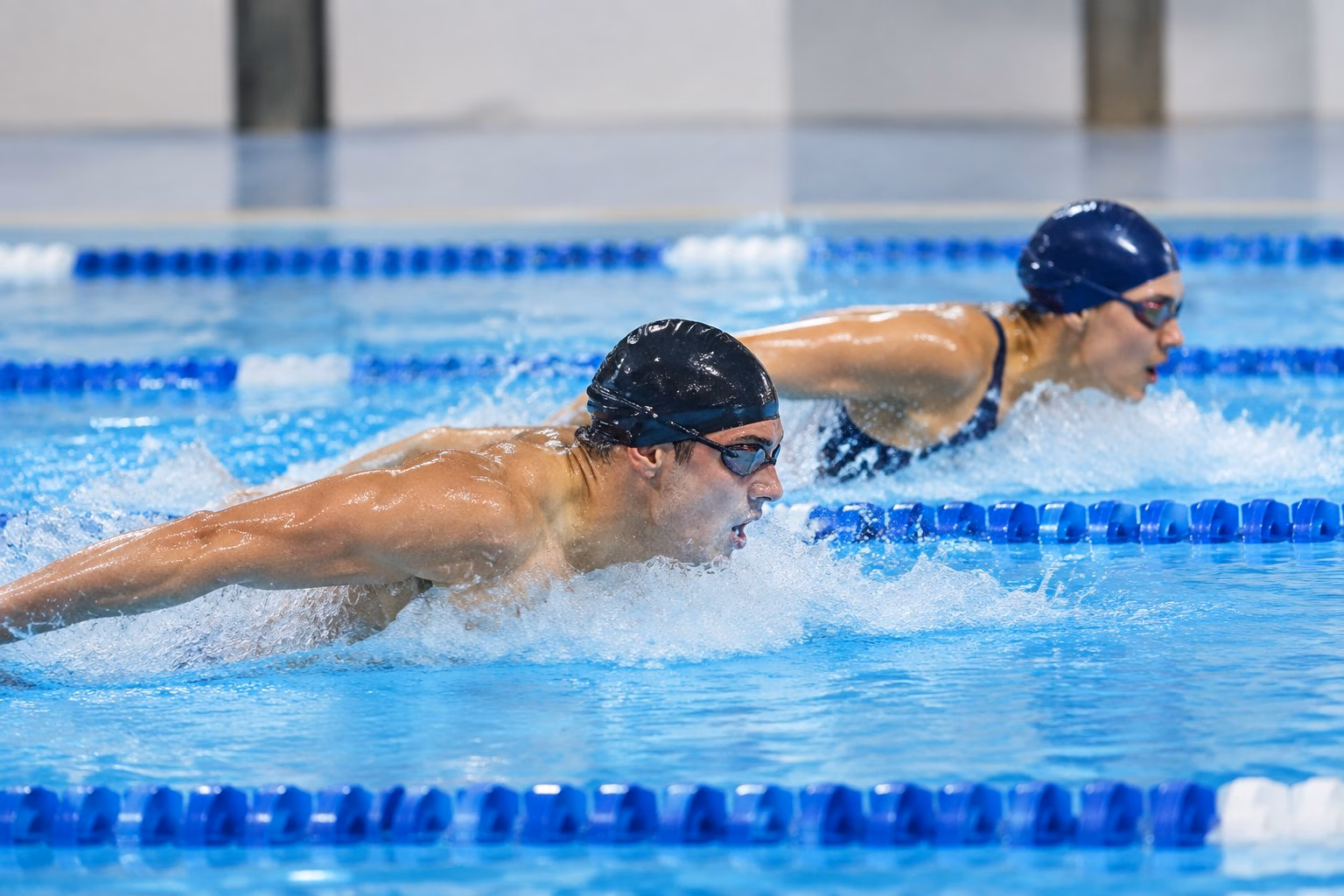 Two swimmers race side by side in an indoor pool.
