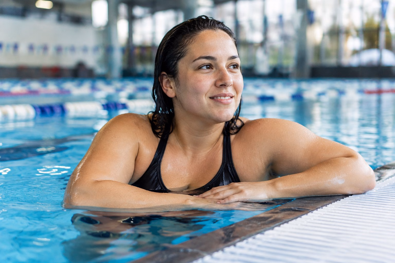 A confident swimmer rests at the edge of an indoor pool.