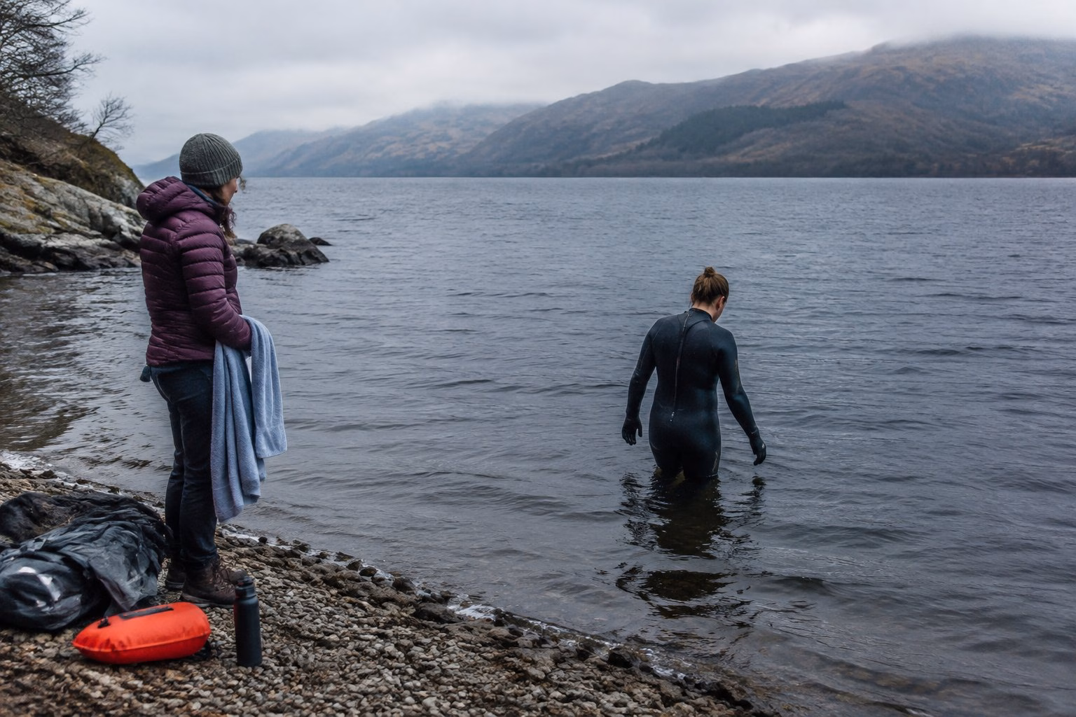 A swimmer cautiously enters Loch Ness while another person waits on the shore.