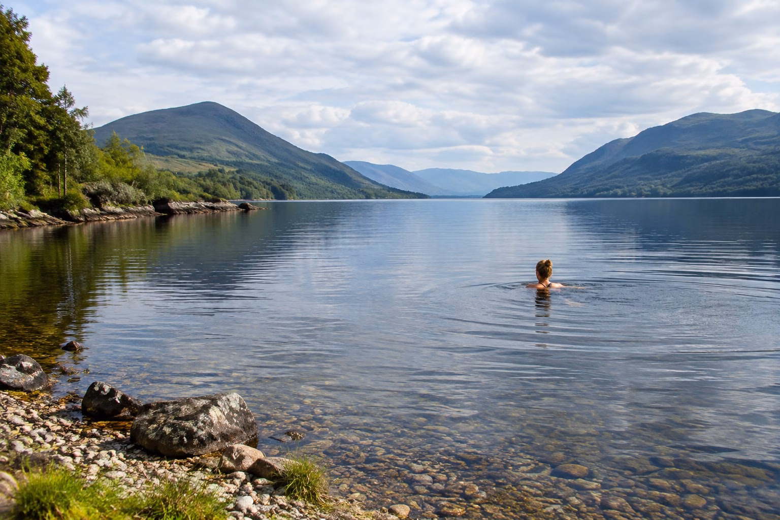 A swimmer in a calm Highland loch with hills in the distance.
